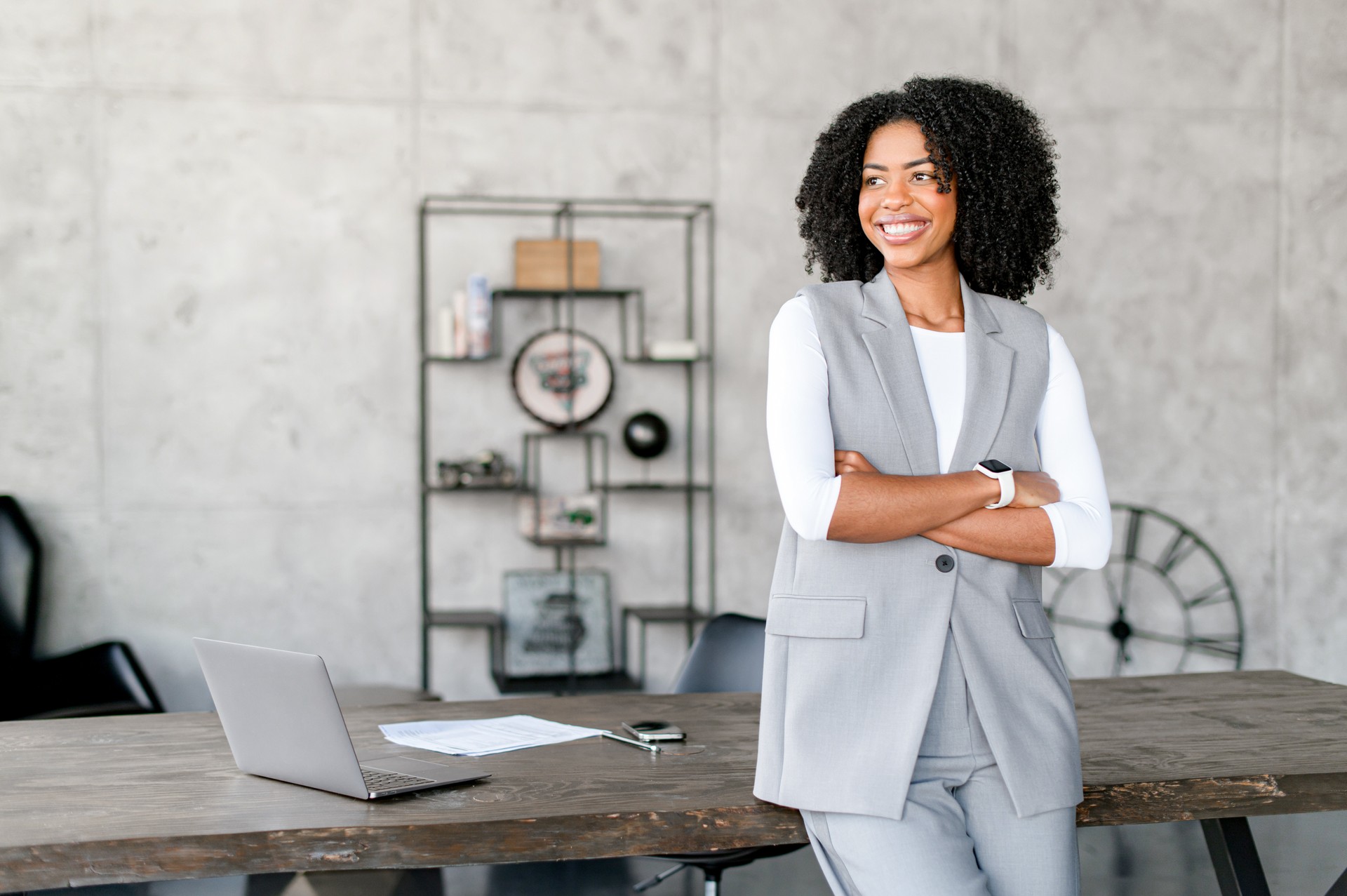 A joyful African-American businesswoman leaning on a desk in office space